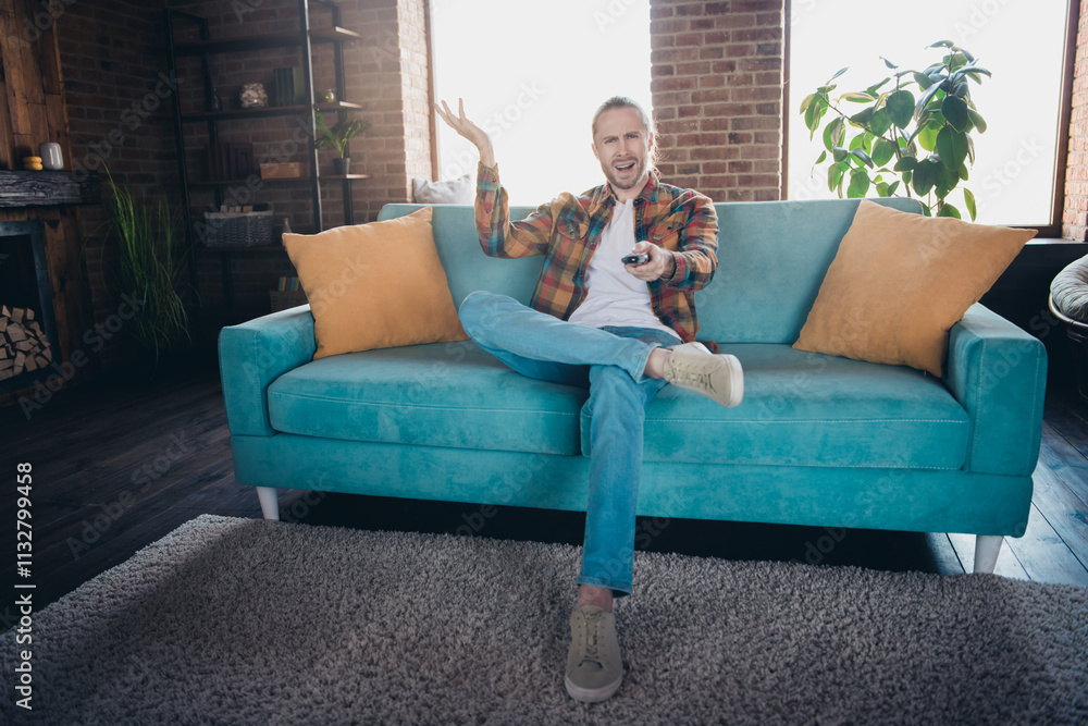 Obraz premium Young man in casual style enjoying a relaxed day indoors on a cozy blue sofa in a stylish loft apartment
