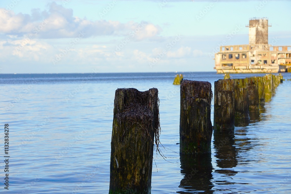 Fototapeta premium Falochron służący do ochrony wybrzeża. Solidny falochron na pierwszym planie, a w tle forteca.