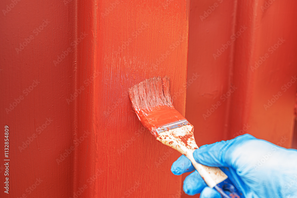 A hand with a brush paints an old iron surface with burgundy paint.
