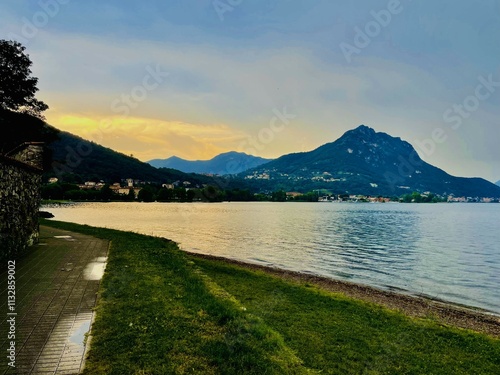 A peaceful lakeside scene during sunset, with golden light illuminating the sky and reflecting on the calm water
