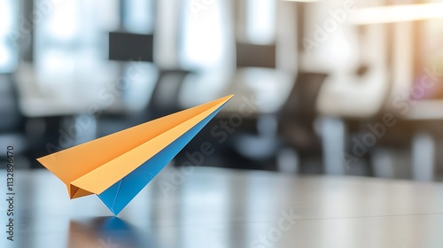 A colorful paper airplane rests on a desk in a modern office space, symbolizing creativity and playfulness in a professional environment.
