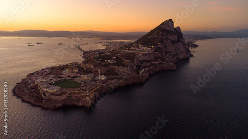 Aerial drone view of Gibraltar at sunset. Street lights on. Europa Sports Complex Stadium. Famous travel destination. Bay of Gibraltar. Orange sunset reflecting on water and landscape. 