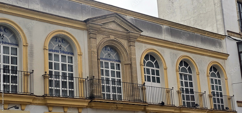 Obraz premium Facade of a historic building with arched windows, wrought iron balconies, and signs indicating tax advisory services; neutral colors and weathered textures on the exterior;