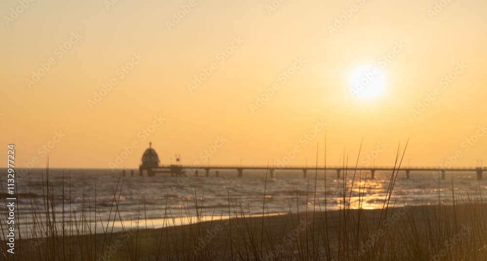 Fototapeta premium Orangener Sonnenaufgang über der Seebrücke Zinnowitz auf Usedom, mit Möwen im Flug über dem Meer.
