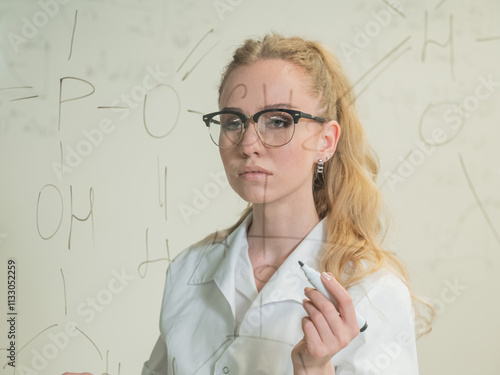 A Caucasian woman in a medical gown thinks and finalizes formulas on a transparent wall.  photo