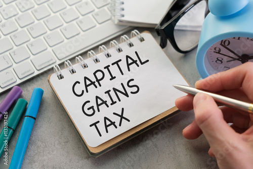 A person is writing on a piece of paper that says Capital Gains Tax photo