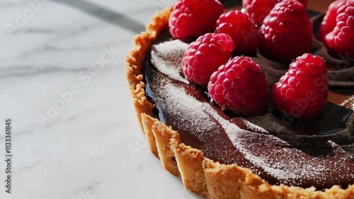 A vegan chocolate tart with a coconut crust, topped with fresh raspberries and a dusting of cocoa powder. photo