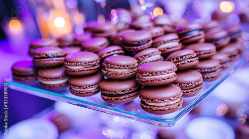 An elegant showcase of chocolate macarons on a glass stand, framed by vivid flowers, at a festive occasion with soft lighting and a warm, inviting atmosphere. photo