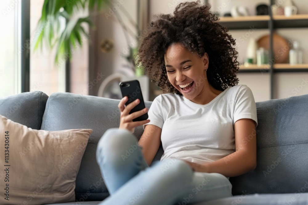 Woman is sitting on a couch and smiling while holding a cell phone. She is looking at the screen of the phone Woman is sitting on a couch and smiling while holding a cell phone. She is looking at the screen of the phone