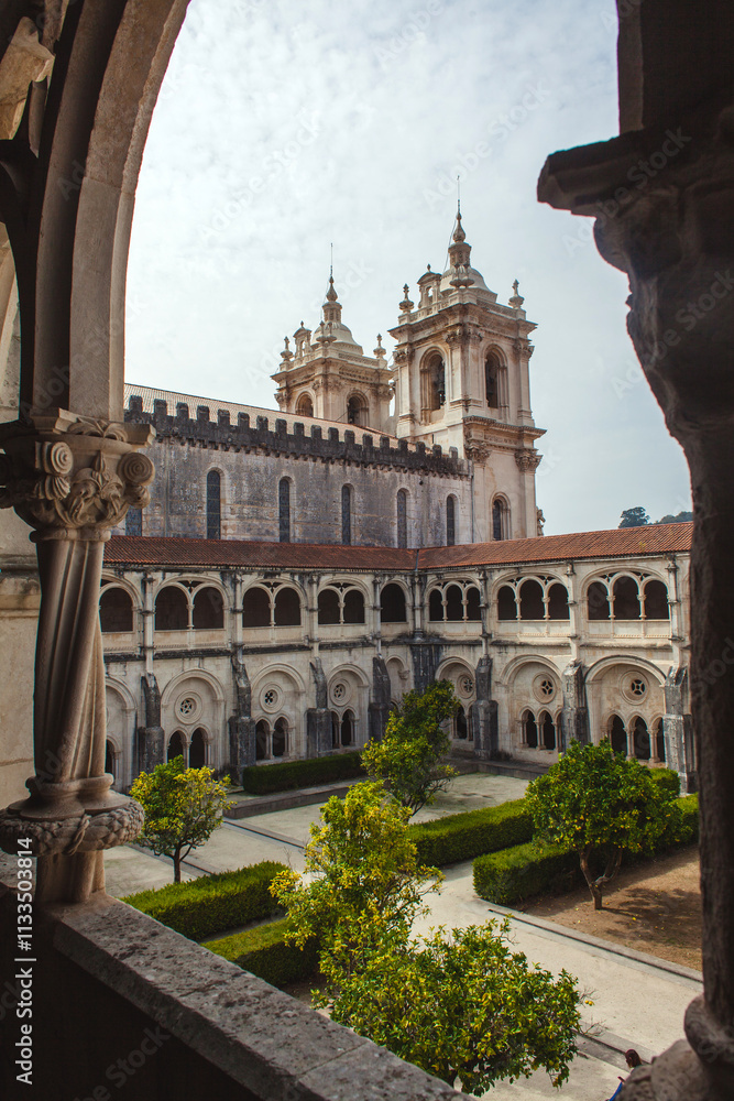 Obraz premium picturesque view through a stone archway, showcasing the architectural grandeur of a historic monastery with its ornate facade, intricate details, and a lush green courtyard