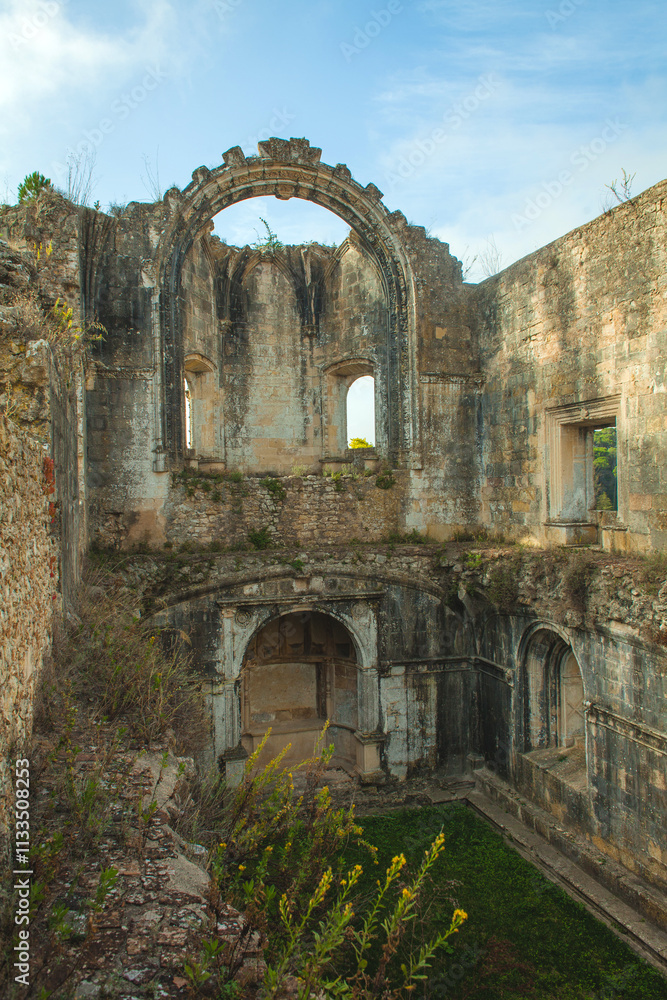 Fototapeta premium ruined interior space with crumbling walls, arched windows, and a patch of vibrant green grass growing within, evoking a sense of history and decay.