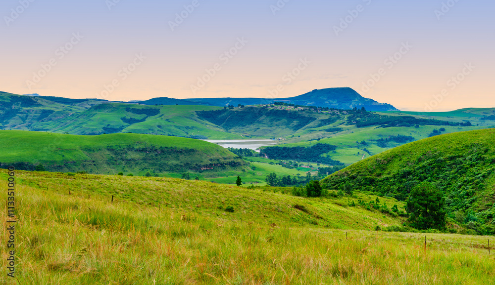 Drakensberg valley with rolling hills and a dam, featuring a village on the hilltop, KwaZulu-Natal, South Africa
