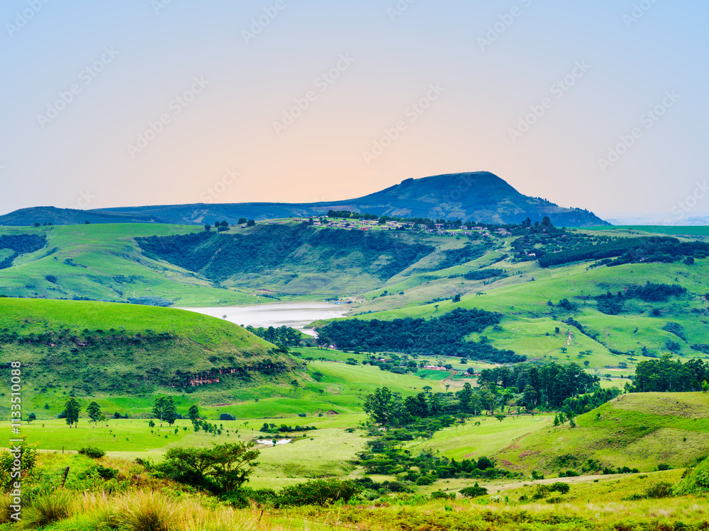 Scenic and tranquil landscape of Drakensberg valley, the dam, and a village on the mountain edge during sunset, KwaZulu-Natal, South Africa