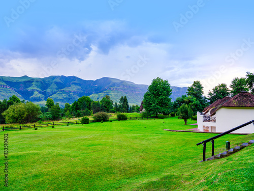 Obraz na płótnie Lush grass field with a thatch-roof house and Drakensberg mountain in the background, KwaZulu-Natal, South Africa w salonie
