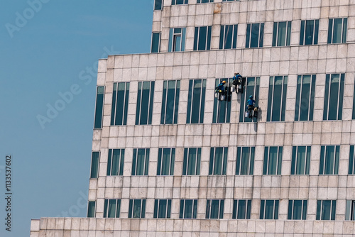 Window washers diligently cleaning a skyscraper facade under a bright, sunny sky, showcasing their skill and teamwork at great heights. Bangkok, Thailand