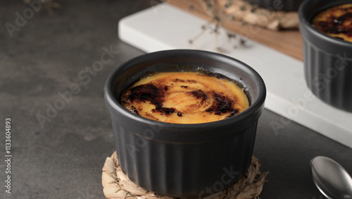 Obraz na plátně Crème brûlée in a black ramekin with a caramelized sugar top, placed on a woven