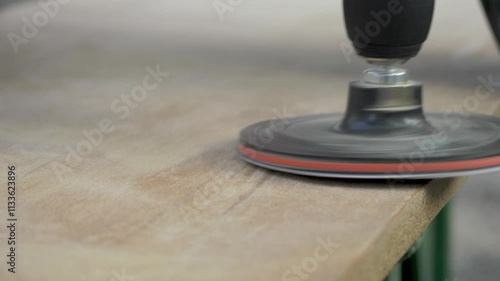 The sander is smoothing a wooden board, making consistent passes across the surface to remove rough spots and create an even texture. Power tool used to smooth surfaces by abrasion with sandpaper photo