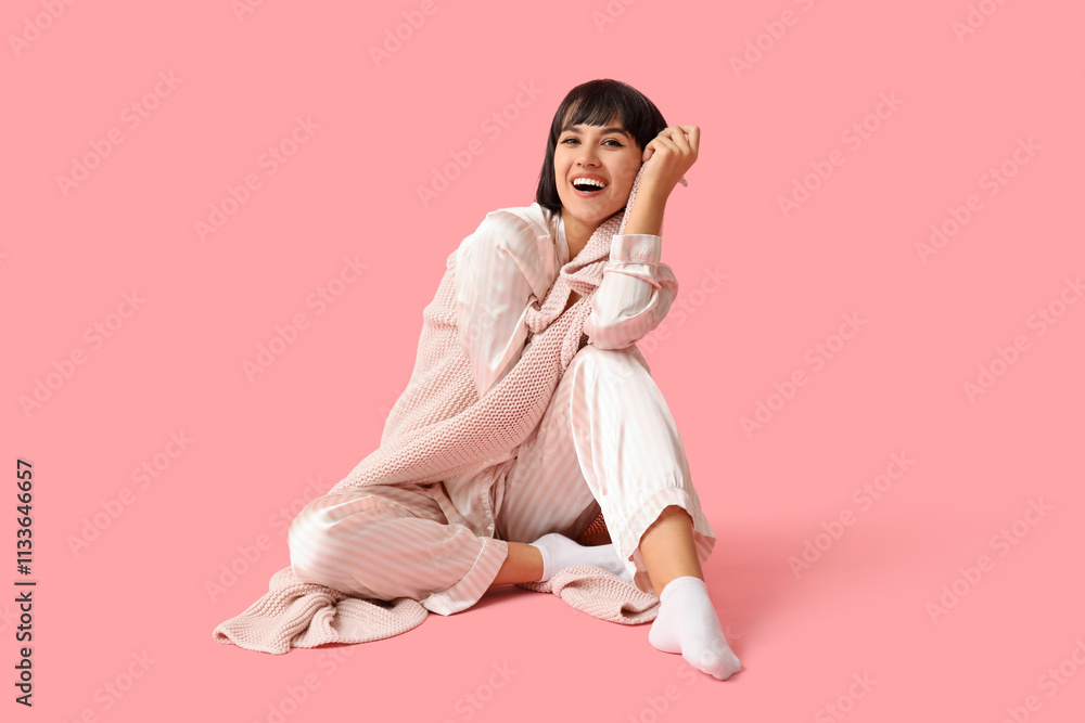 Happy young woman in pajamas with plaid sitting on pink background Happy young woman in pajamas with plaid sitting on pink background
