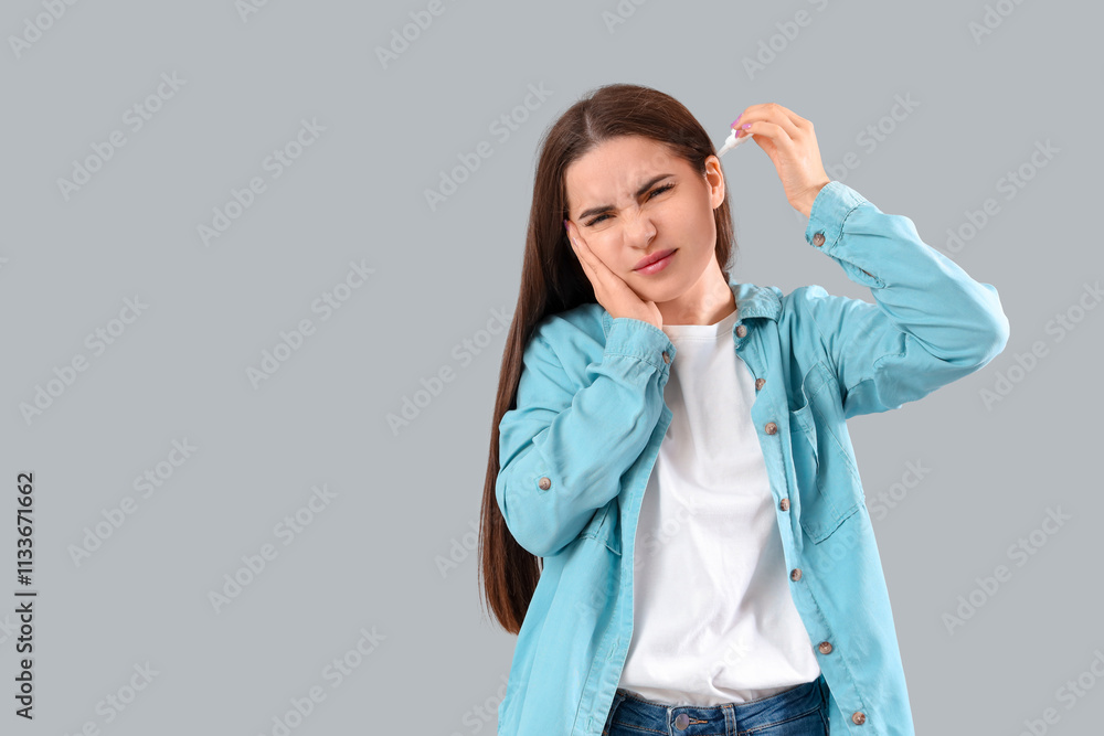 Young woman with otitis using ear drops on grey background Young woman with otitis using ear drops on grey background