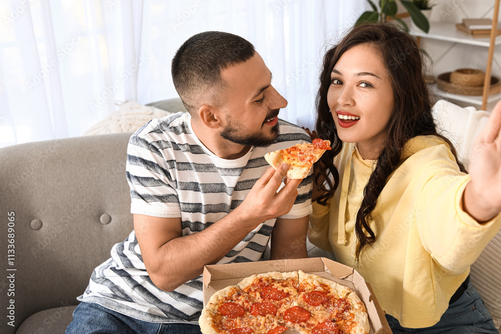 Young couple with pepperoni pizza taking selfie on sofa at home