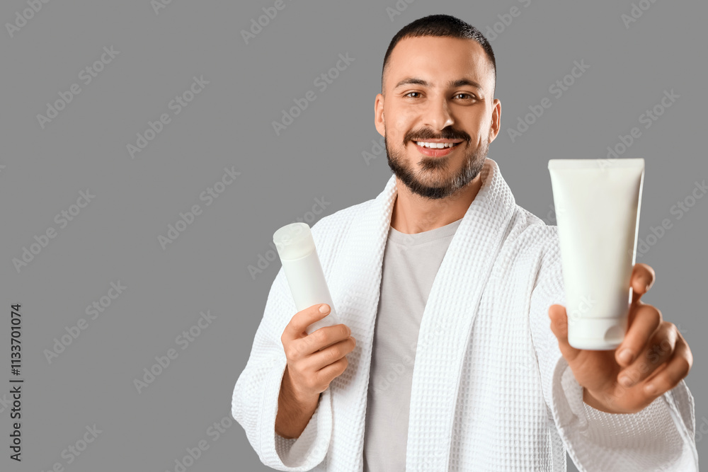 Young man in robe with skin care cosmetics on grey background Young man in robe with skin care cosmetics on grey background