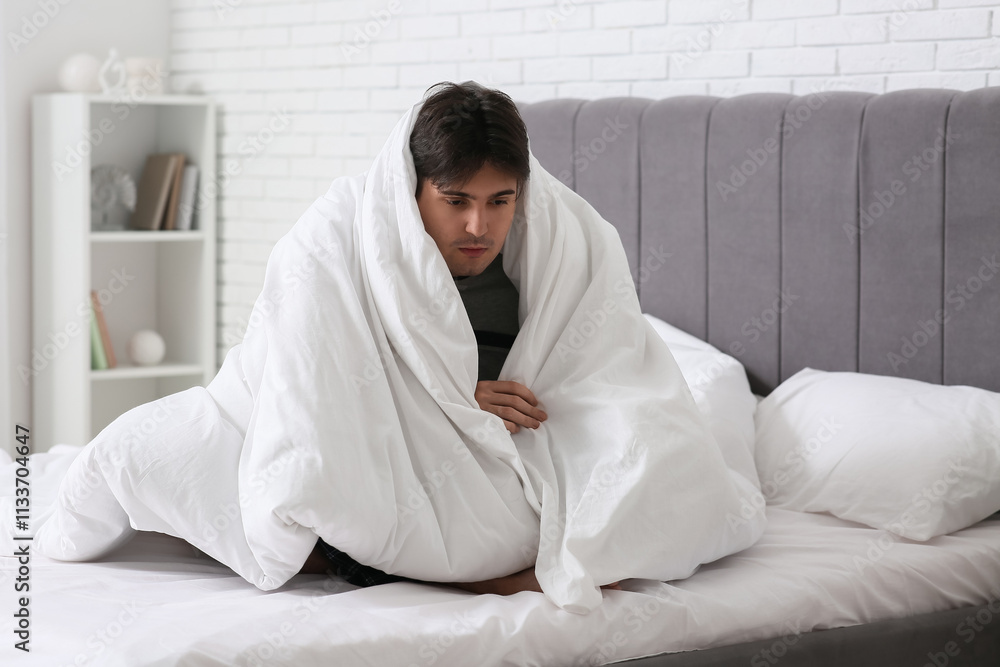 Depressed young man with blanket sitting in bedroom Depressed young man with blanket sitting in bedroom