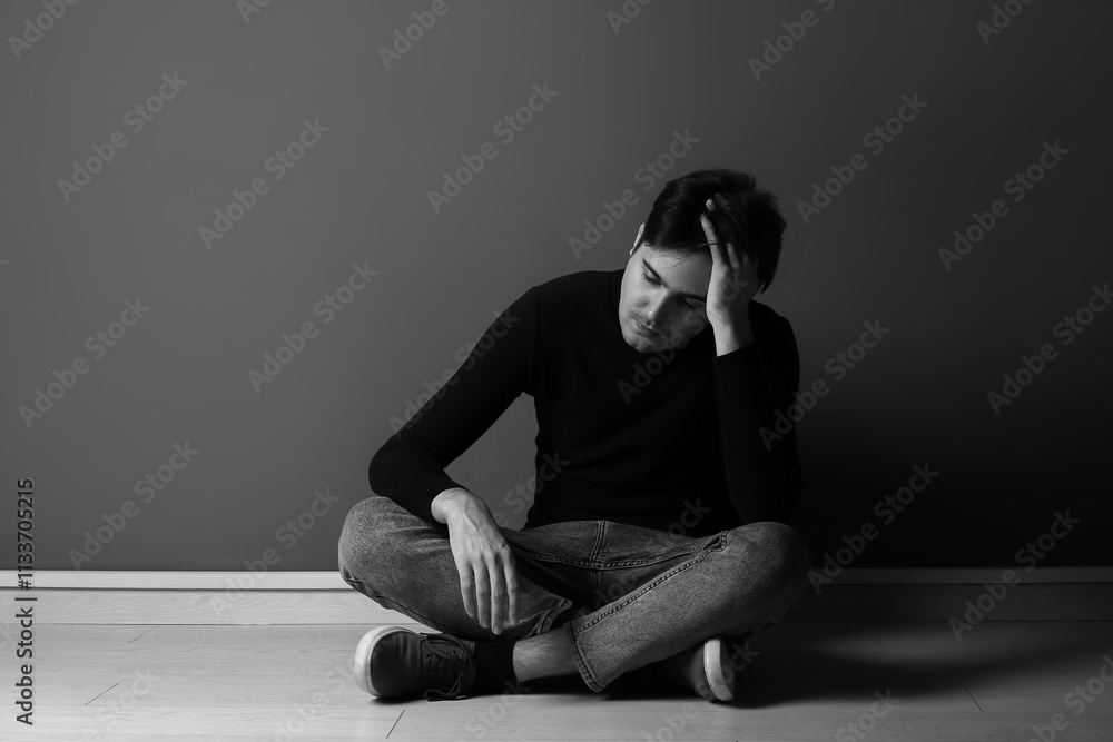 Black and white portrait of depressed young man sitting near dark wall Black and white portrait of depressed young man sitting near dark wall