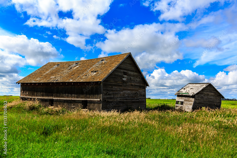 A large, old barn sits in a field with a cloudy sky overhead A large, old barn sits in a field with a cloudy sky overhead