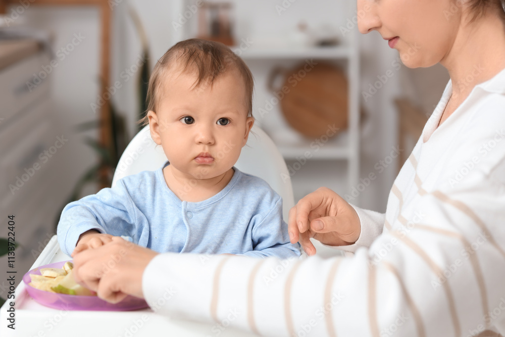 Cute little baby with fruits in high chair and mother at home Cute little baby with fruits in high chair and mother at home
