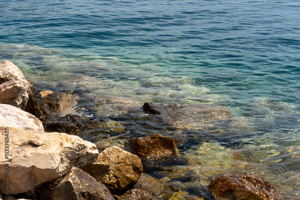 Clear turquoise water washing over rocky coastline with sunlight creating sparkling reflections. Concept of natural beauty, coastal landscapes, and peaceful outdoor scenery. Clear turquoise water washing over rocky coastline with sunlight creating sparkling reflections. Concept of natural beauty, coastal landscapes, and peaceful outdoor scenery.
