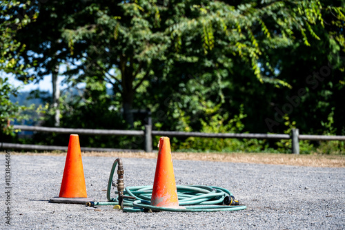  Gravel maintenance yard in public park with irrigation pipe spigot and green garden hose coiled up with orange safety cones protecting it, grounds keeping in progress
 photo