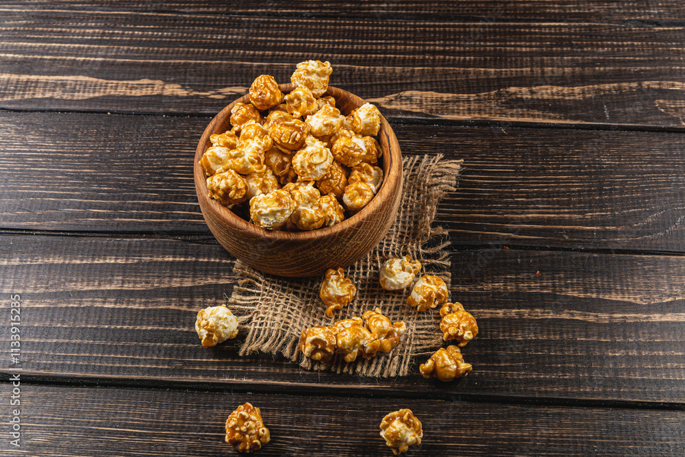 Fototapeta premium Snack, movie concept, caramelized popcorn in a wooden bowl on a wooden table