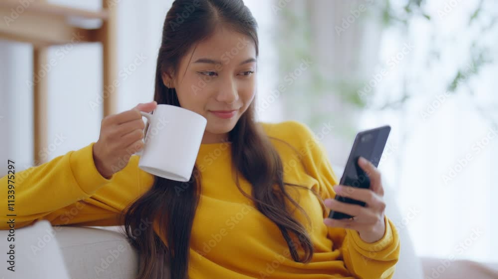 Happy young asian woman relax on comfortable couch at home texting messaging on smartphone, smiling girl use cellphone chatting, browse wireless internet on gadget, shopping online from home Happy young asian woman relax on comfortable couch at home texting messaging on smartphone, smiling girl use cellphone chatting, browse wireless internet on gadget, shopping online from home