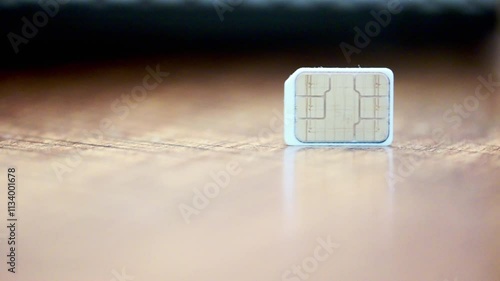 A cell phone battery is sitting on a wooden table. The battery is small and white. The table is made of wood and has a natural grain. The scene is simple and uncluttered