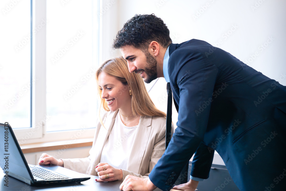 Fototapeta premium Professional man and woman working together on a laptop in a modern office. The woman points at the screen, explaining details while the man listens attentively.