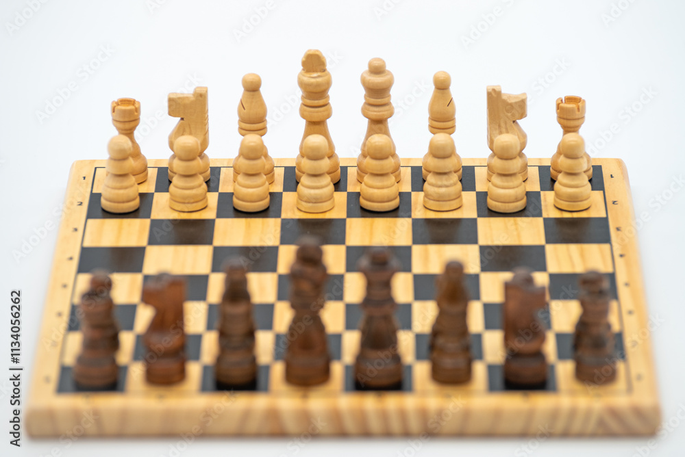 Wooden chessboard with pieces in initial positions from the black side. White pieces in focus. Isolated on white background. Wooden chessboard with pieces in initial positions from the black side. White pieces in focus. Isolated on white background.