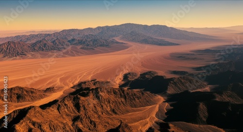 Rocky desert landscape with distant mountains under an orange sky