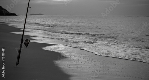 High resolution image in black and white of a single fishing rod with a beautiful beach background during sunset