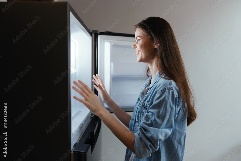 Young woman in denim shirt joyfully looking into an open refrigerator, showcasing healthy eating habits and a vibrant lifestyle Young woman in denim shirt joyfully looking into an open refrigerator, showcasing healthy eating habits and a vibrant lifestyle