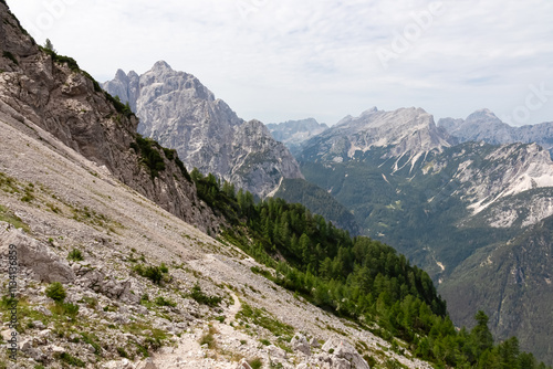 Hiking trail through scree field with panoramic view of rugged mountain ridge Prisank in majestic Julian Alps. Hike adventure in Triglav National Park, Slovenia, Slovenian Alps. Jagged alpine terrain