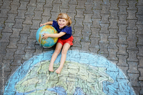 Little preschool girl with earth globe painting with colorful chalks on ground. Positive toddler child. Happy earth day concept. Creation of children for saving world, environment and ecology.
