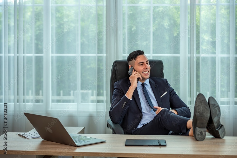 Confident businessman in suit talking on the phone and relaxing with feet on desk in modern office. Confident businessman in suit talking on the phone and relaxing with feet on desk in modern office.