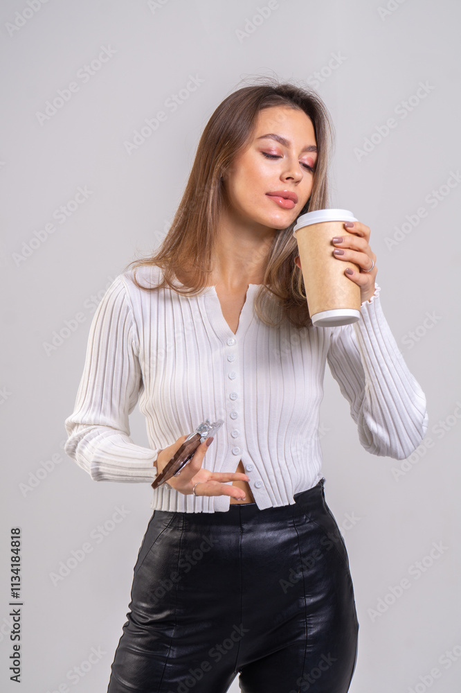 Attractive brunette young woman holding a cofee cup and chocolate on a white background. Copy space, close-up portrait Attractive brunette young woman holding a cofee cup and chocolate on a white background. Copy space, close-up portrait