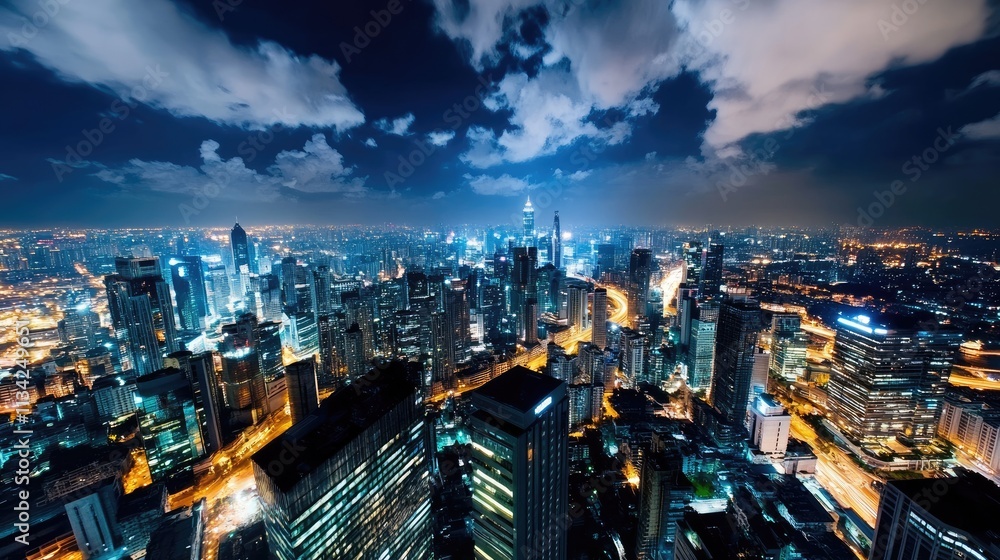 Obraz premium Stunning Aerial Night View of a Modern Cityscape with Illuminated Skyscrapers and Vibrant Urban Lights Under a Dramatic Cloudy Sky