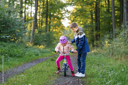 Cute little preschool girl in safety helmet riding bicycle. School kid boy, brother teaching happy healthy sister child cycling and having fun with learning bike. Active siblings family outdoors. photo