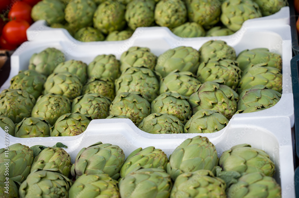 Fototapeta premium a bunch of green artichoke are stacked on white plastic containers.