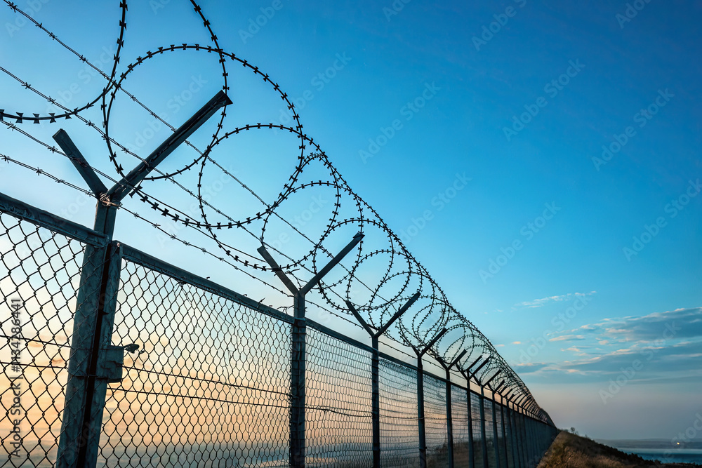 Fence With Barbed Wire in Front of a Great Blue Sky - Concept of Freedom, Liberty, or Confinement Fence With Barbed Wire in Front of a Great Blue Sky - Concept of Freedom, Liberty, or Confinement