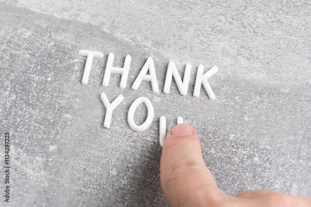 Fototapeta premium White letters forming word thank you on gray concrete background.