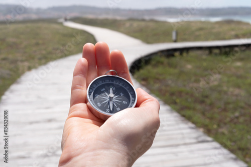 A person holding a compass on a wooden boardwalk. The compass is pointing to the right.