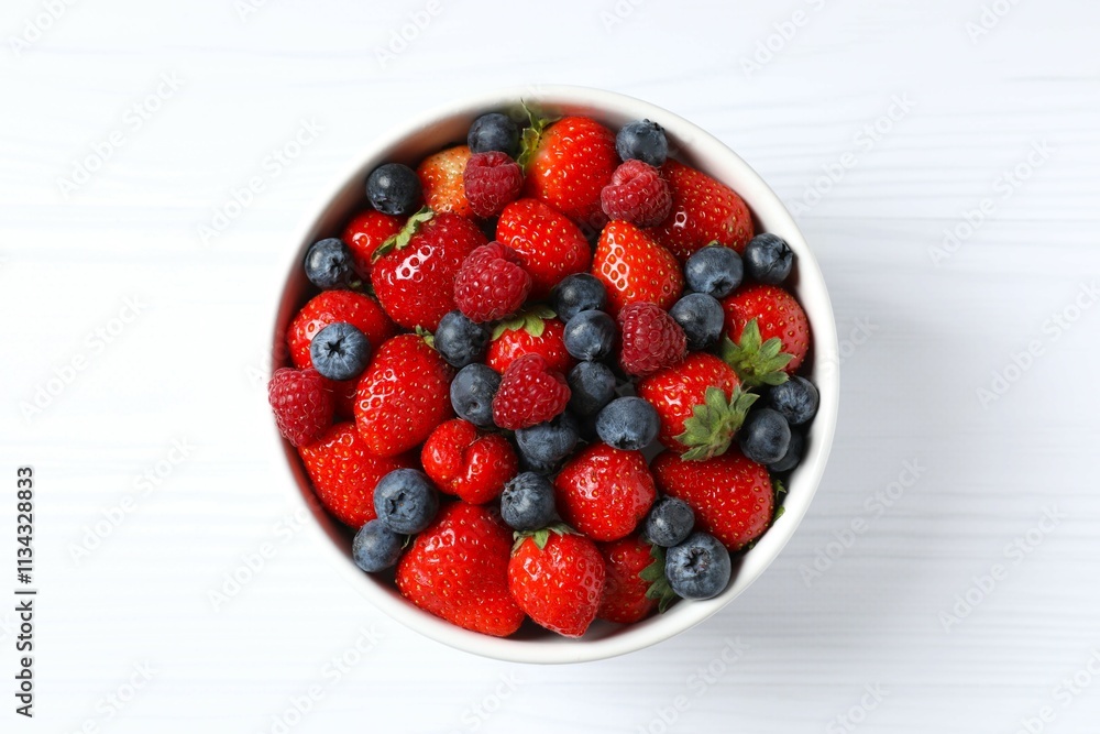 Different fresh ripe berries in bowl on wooden table, top view Different fresh ripe berries in bowl on wooden table, top view